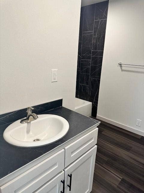 1613 Campbell Street, #A, Commerce, TX 75428 Bathroom featuring white cabinetry with matte black hardware, dark stone-finish countertop with an undermount sink, wood-finish flooring, and a tub enclosure accented with floor-to-ceiling dark stone-finish wall tile