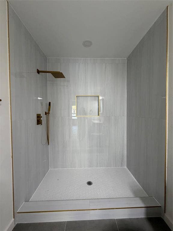 Walk-in shower featuring floor-to-ceiling neutral tile, rainfall showerhead with secondary handheld sprayer, gold-toned hardware, and a built-in tiled wall niche