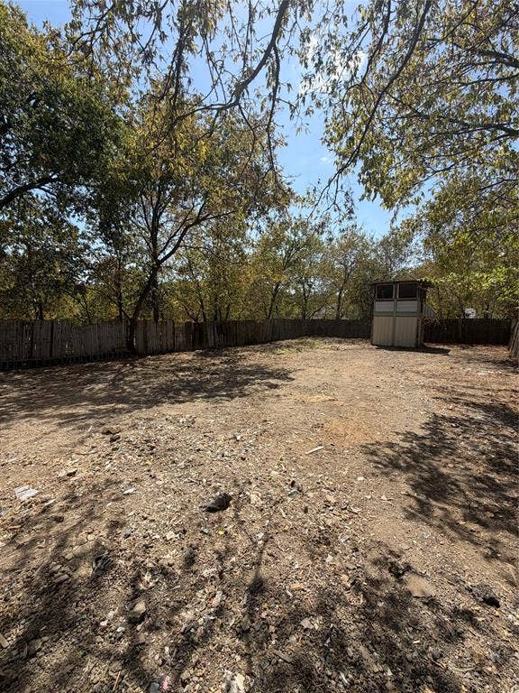 Open outdoor area enclosed by a wood-slat perimeter fence with mature trees and a detached storage structure