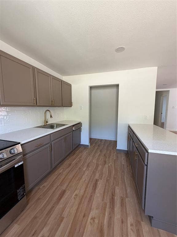 Kitchen featuring shaker-style cabinetry, white countertops, a subway tile backsplash, a stainless steel undermount sink with a high-arch faucet, and wood-finish flooring
