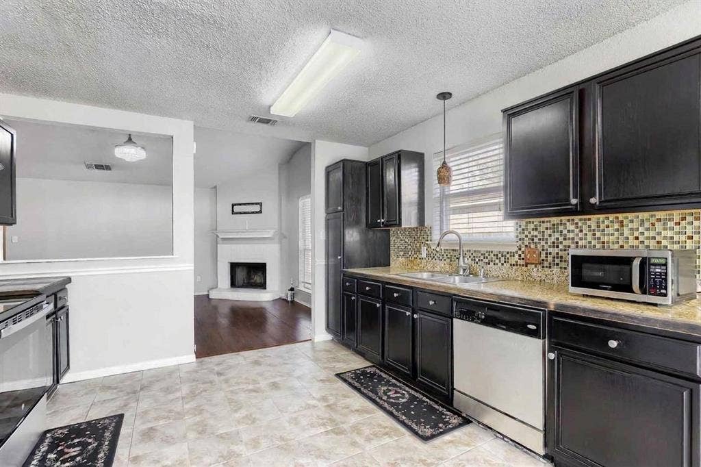 2039 Angelica Way, Dallas, TX 75217 Kitchen featuring dark wood cabinetry, stone-finish countertops, decorative tile backsplash, stainless steel dishwasher, and tile flooring