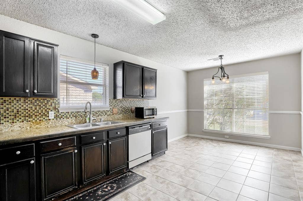 2039 Angelica Way, Dallas, TX 75217 Kitchen featuring dark-finish cabinetry, stone-texture countertops, mosaic tile backsplash, integrated stainless steel dishwasher, and ceramic tile flooring
