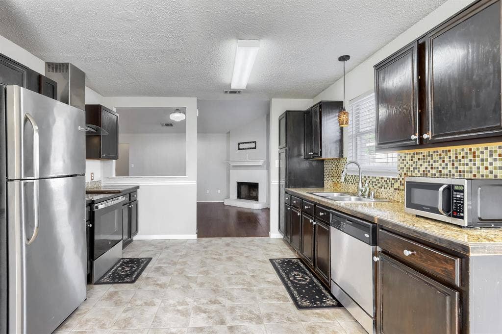 2039 Angelica Way, Dallas, TX 75217 Kitchen featuring dark-finish cabinetry, stone-texture countertops, mosaic tile backsplash, stainless steel appliances, and tile flooring