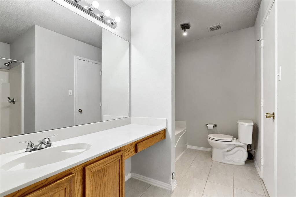2039 Angelica Way, Dallas, TX 75217 Full-width vanity with integrated sink, wood-finish cabinetry, expansive wall-mounted mirror, ceramic tile flooring, and separate water closet area