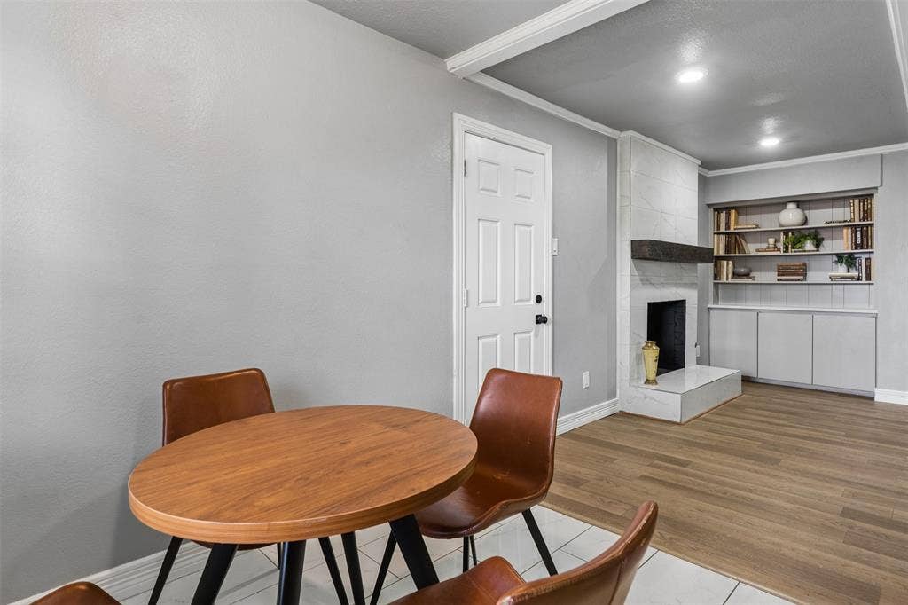 Fireplace featuring a light-toned stone surround, raised hearth, and dark wood mantel, complemented by built-in cabinetry and recessed shelving, wood-finish flooring, and recessed ceiling lighting