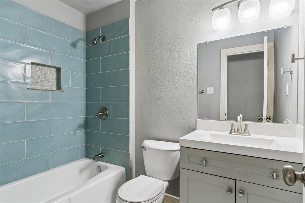 Bathroom featuring a gray vanity with a white countertop, inset sink, large rectangular wall mirror, blue subway-tile shower surround with a built-in recessed niche, and three-light wall-mounted fixture