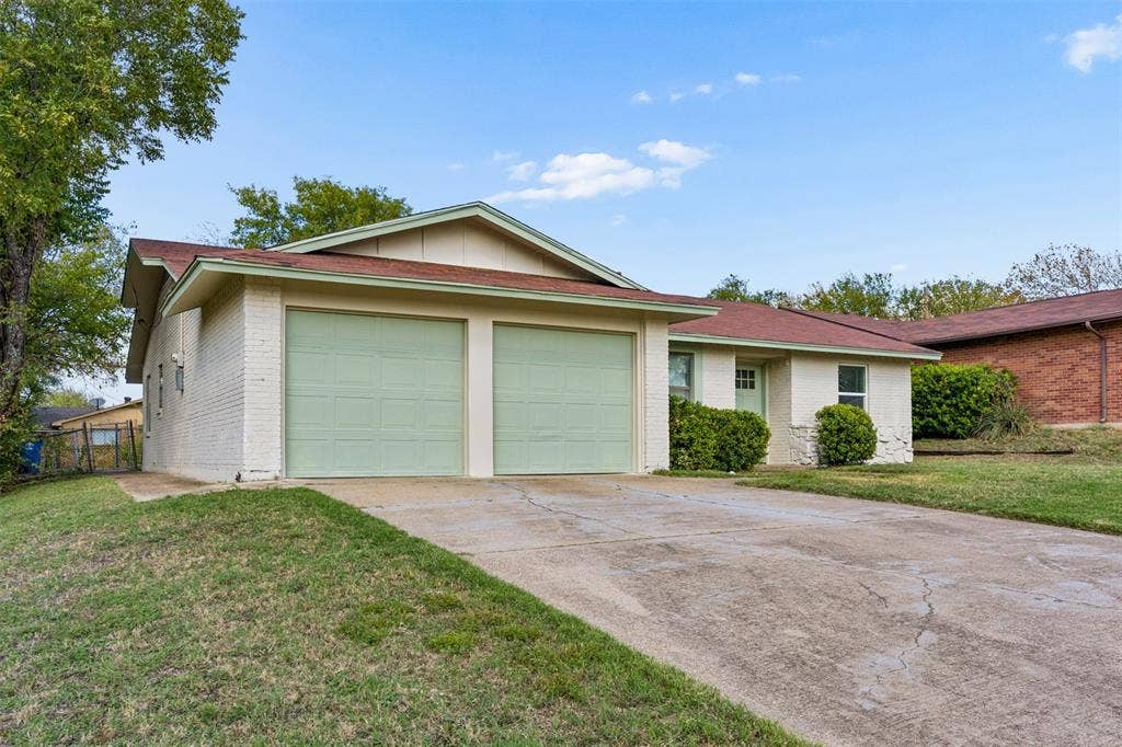 Light-colored brick exterior featuring a low-pitched roof, attached two-car garage, and concrete driveway