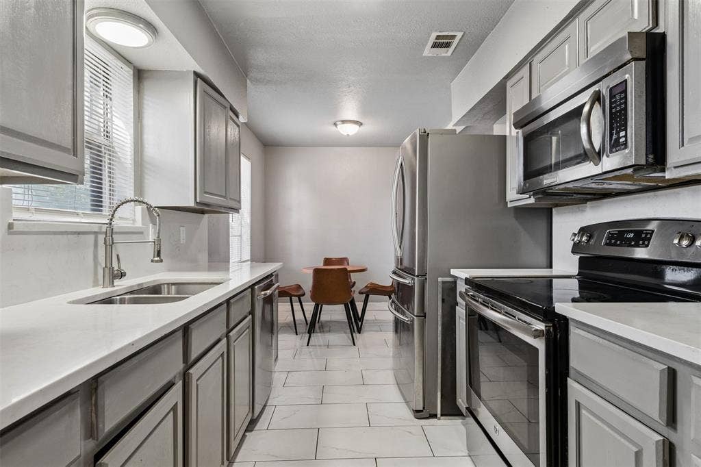 Kitchen featuring gray cabinetry, solid-surface countertops, tile flooring, and stainless steel appliances including a built-in microwave and range