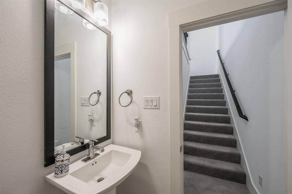 Powder room features a pedestal sink with chrome faucet, black-framed mirror