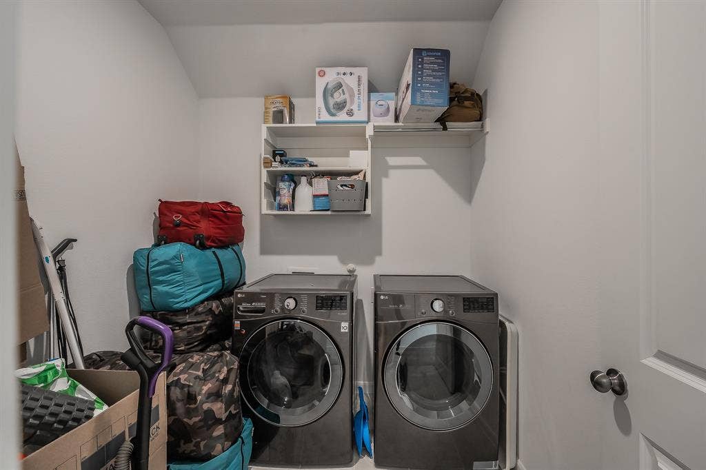 Spacious second floor laundry area featuring built-in shelving, hanging rod, and charcoal-finish front-loading washer and dryer and space for more storage area
