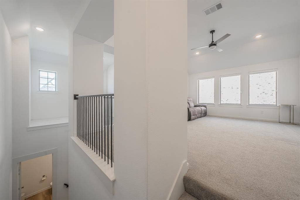 Open-concept loft area featuring a vaulted ceiling, recessed lighting, carpeted flooring, metal balustrade railing, and multiple windows, perfect for multiple uses