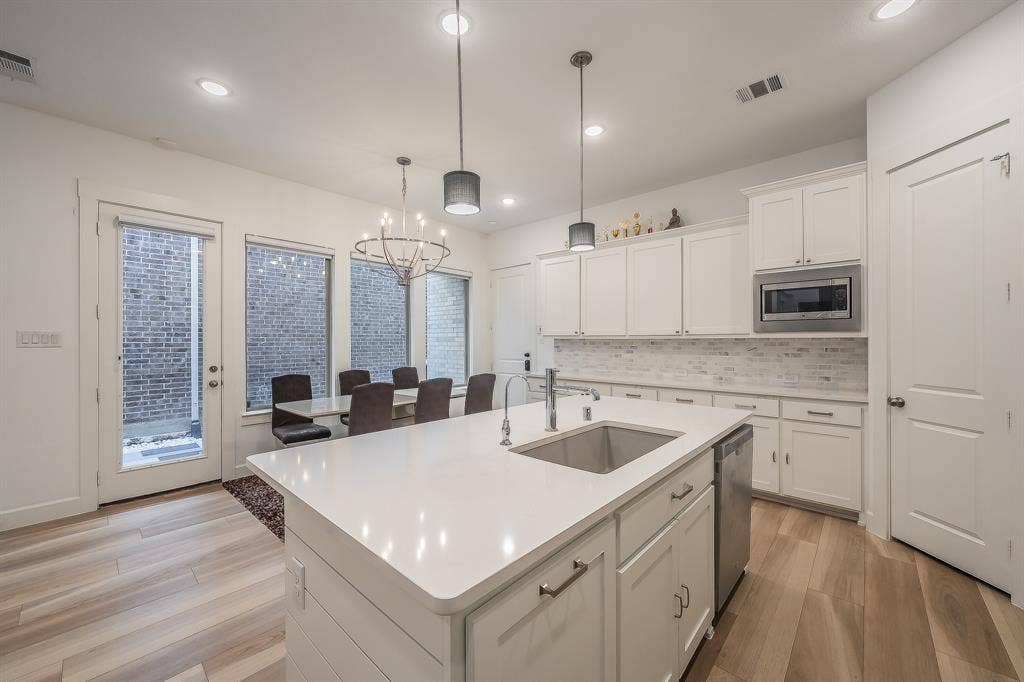 Kitchen featuring white cabinetry, quartz countertops, an oversized central island with an undermount sink, recessed lighting, and wood-finish durable LVP flooring
