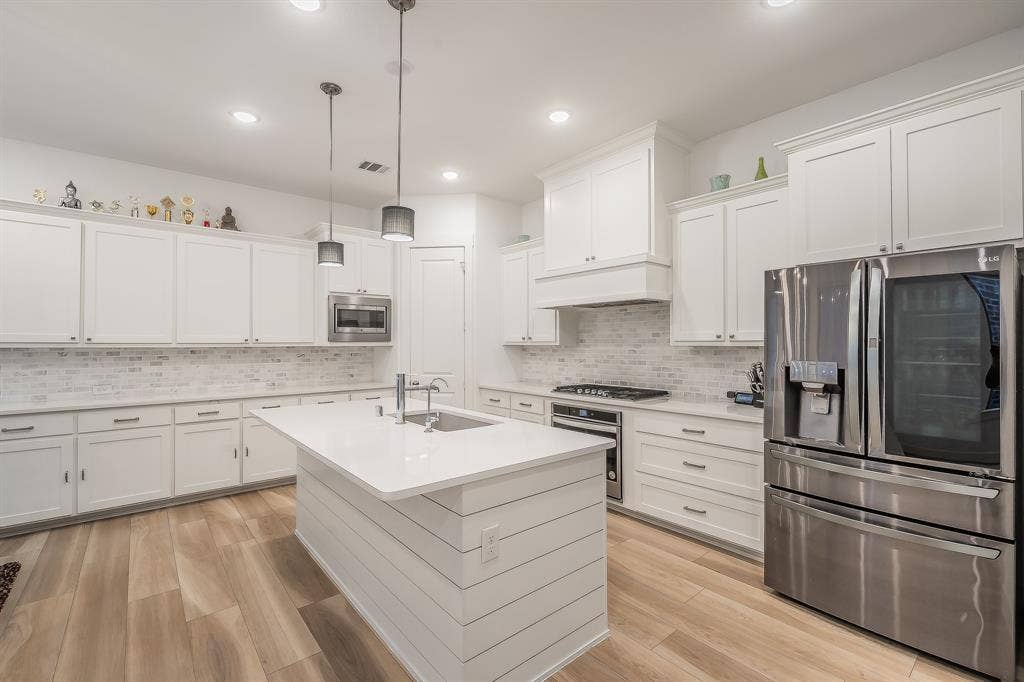 Kitchen featuring white cabinetry, wood-finish flooring, a central island with a quartz countertop, a white brick-pattern backsplash, and stainless steel appliances
