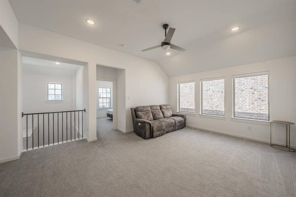 Vaulted ceiling with a ceiling fan, recessed lighting, carpeted flooring, and a metal spindle railing overlooking the lower level, perfect as a game room, secondary living room, or other functional use