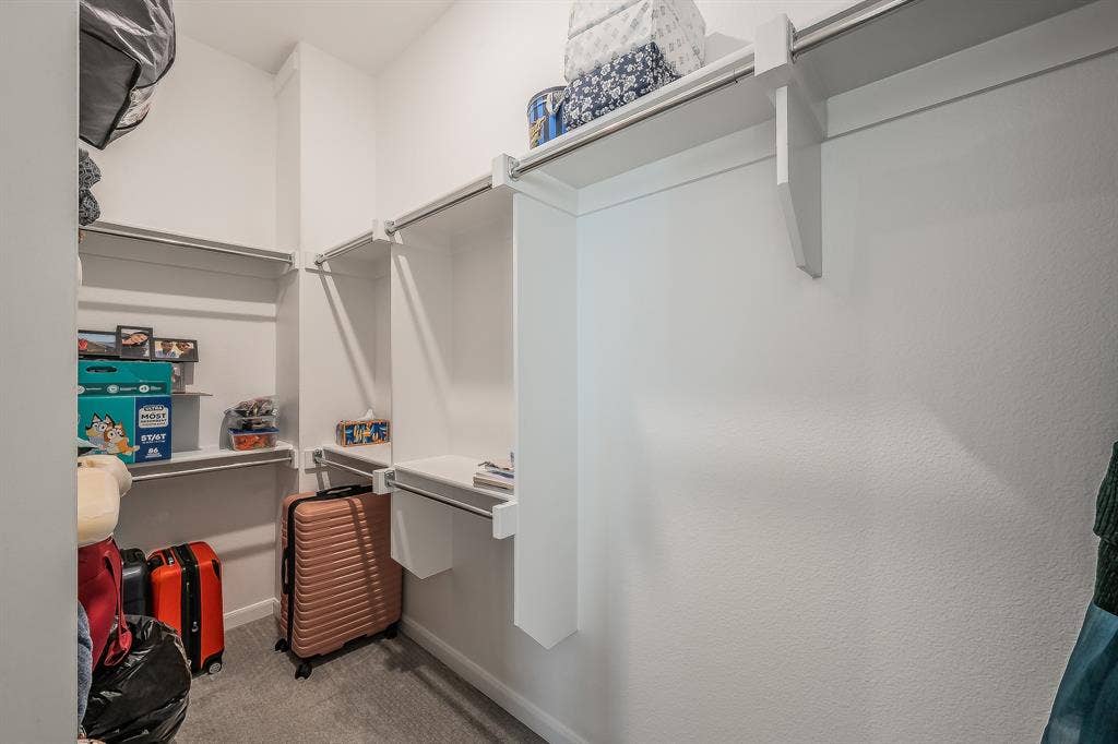 First of two walk-in closets in the primary suite featuring white built-in shelving, integrated hanging rods, and neutral carpeted flooring