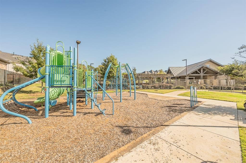 Second of two community playground areas featuring a multi-level structure with slide, climbing apparatus, mulch surfacing, and paved pathways near pool