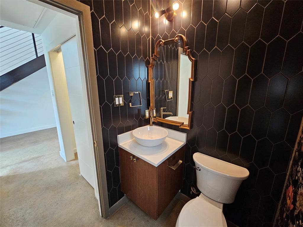 4215 Roseland Avenue, Dallas, TX 75204 Dark hexagonal wall tiling paired with a wood-finish floating vanity, white stone-surface countertop, white vessel sink, and gold-toned wall-mounted lighting