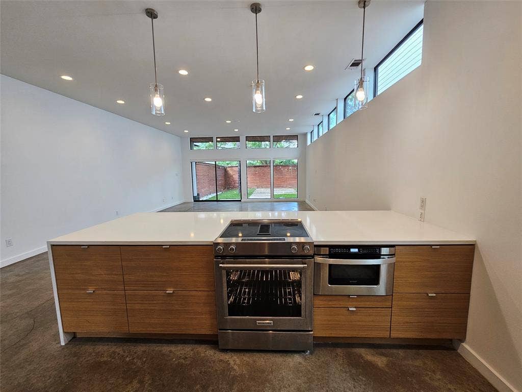 4215 Roseland Avenue, Dallas, TX 75204 Kitchen island featuring wood-finish flat-panel cabinetry, a solid surface countertop, stainless steel slide-in range, built-in microwave, and three glass pendant lights