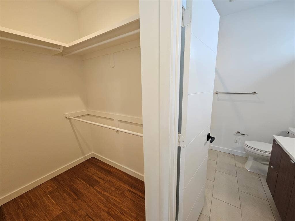4215 Roseland Avenue, Dallas, TX 75204 Walk-in closet featuring tiered shelving and hanging rods, wood-finish flooring, and a multi-panel door leading to a bathroom with tile flooring, a vanity with stone-surface countertop, and a wall-mounted towel bar