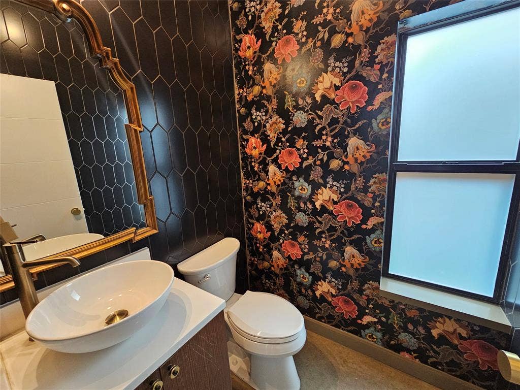 4215 Roseland Avenue, Dallas, TX 75204 Vessel sink with a brass-finish faucet, black hexagonal tile wall, gold-tone ornate mirror, and floral-patterned wall covering
