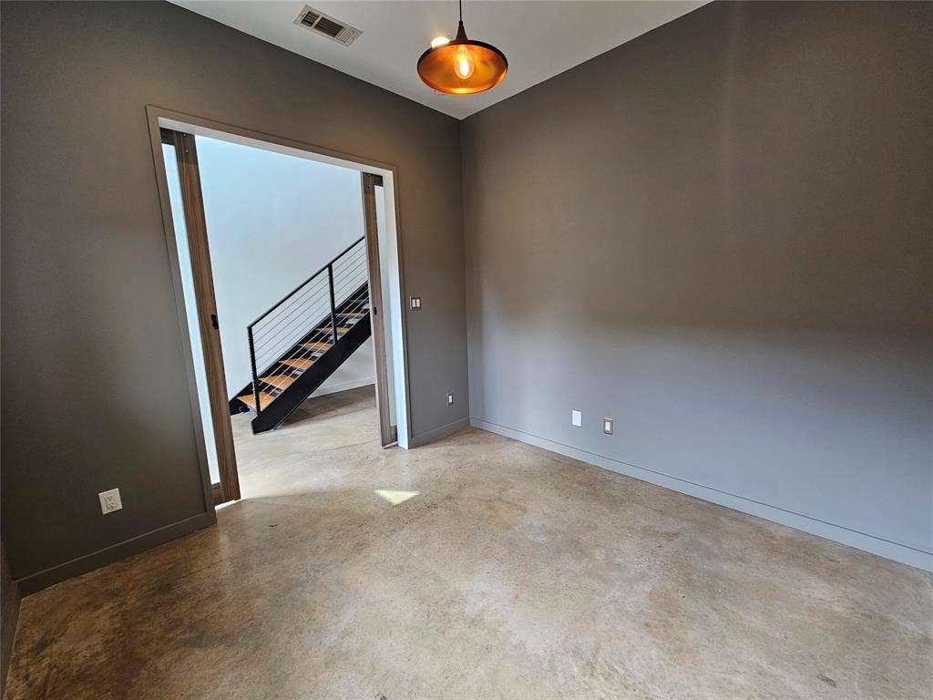 4215 Roseland Avenue, Dallas, TX 75204 Room with stained concrete flooring, dark-toned walls, and a recessed ceiling light, featuring wood-framed sliding pocket doors opening to a staircase with metal railings