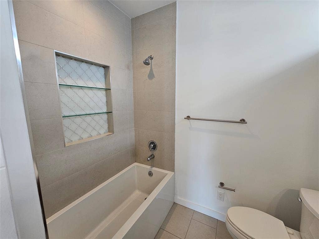 4215 Roseland Avenue, Dallas, TX 75204 Bathtub with tiled surround, recessed wall niche featuring glass shelving, chrome shower fixtures, and stainless steel hardware