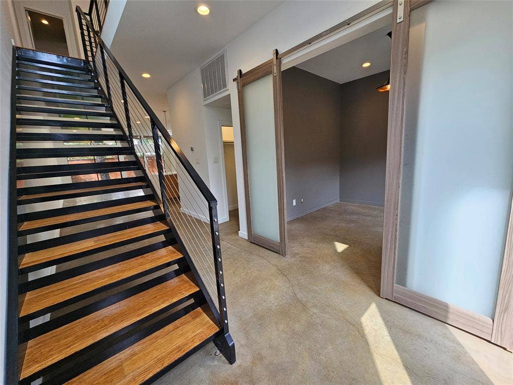 4215 Roseland Avenue, Dallas, TX 75204 Staircase featuring wood-finish treads and metal railings with cable balusters, paired with a sliding frosted glass barn door and concrete flooring