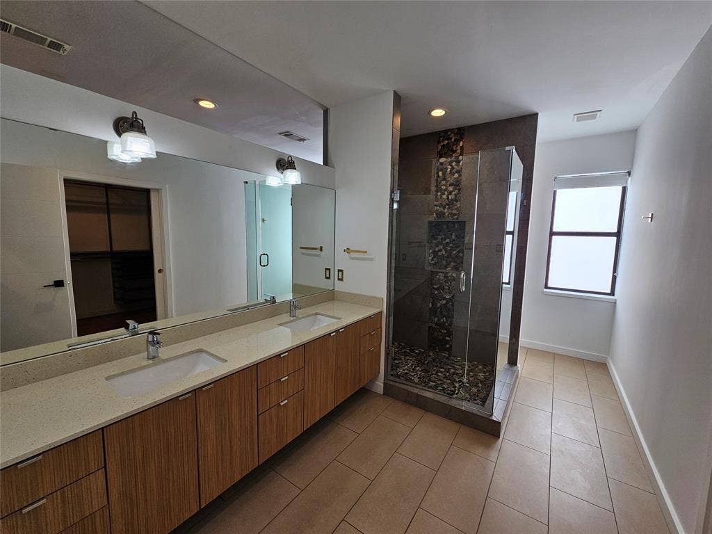 4215 Roseland Avenue, Dallas, TX 75204 Dual-sink vanity with light-tone countertop, wood-finish cabinetry, full-width wall mirror, and walk-in glass shower featuring an accent tile inlay