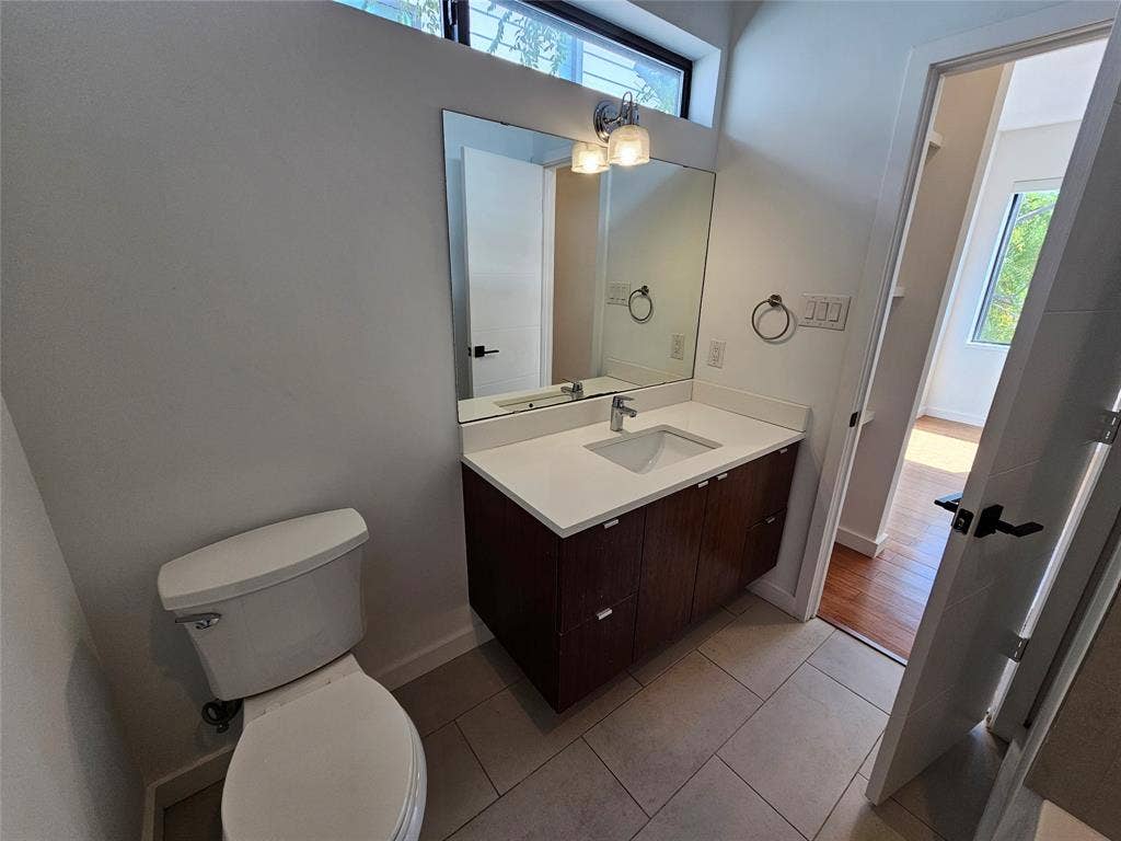4215 Roseland Avenue, Dallas, TX 75204 Floating vanity featuring a dark wood-finish cabinet, white solid-surface countertop, rectangular undermount sink, and polished chrome fixtures, complemented by tile flooring and a high-set transom window