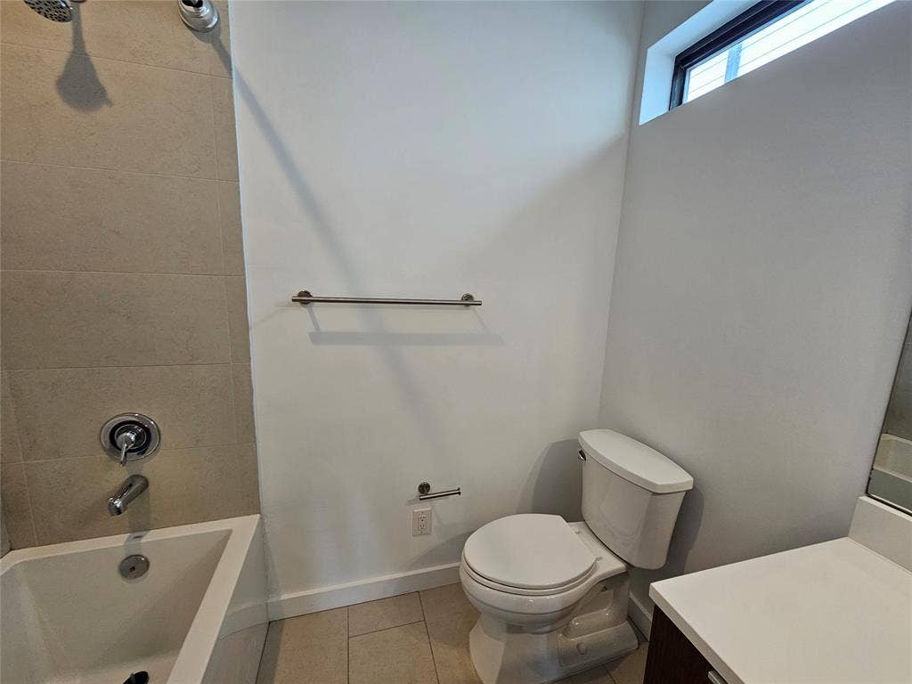 4215 Roseland Avenue, Dallas, TX 75204 Bathroom featuring a soaking tub with neutral tile surround, a built-in vanity with a solid-surface countertop, high-reach horizontal transom window, and brushed metal fixtures