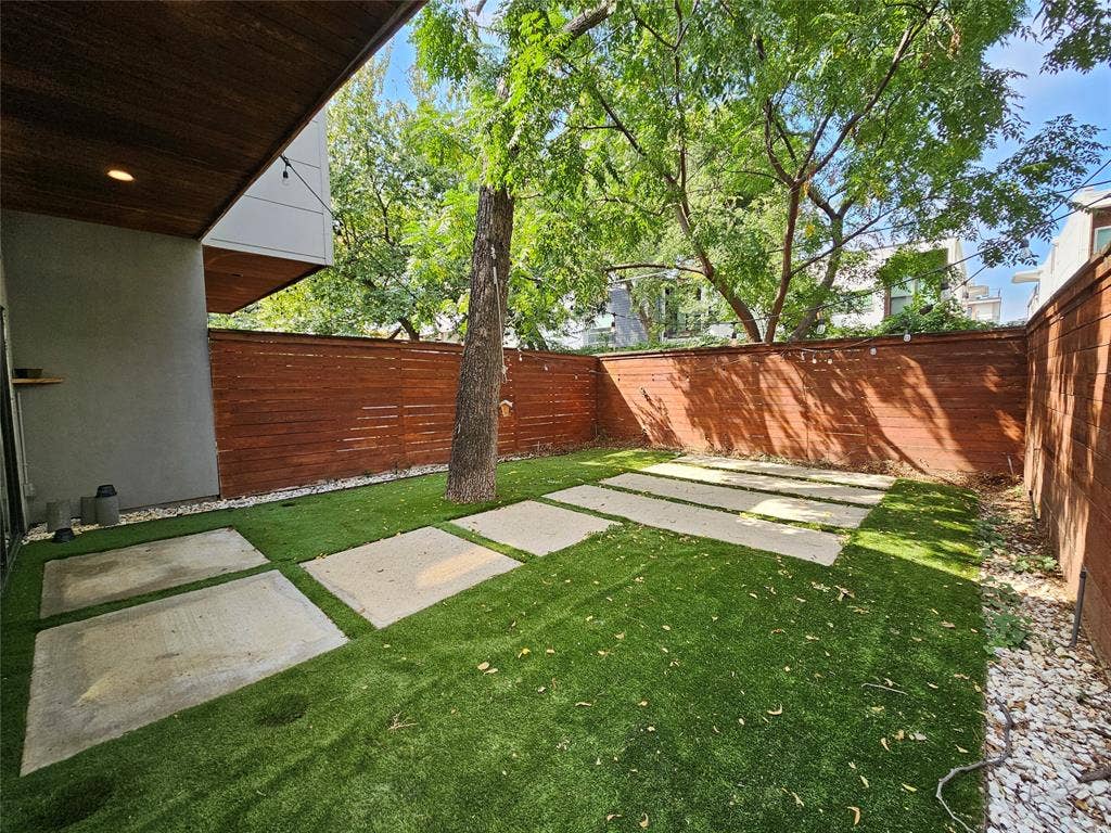 4215 Roseland Avenue, Dallas, TX 75204 Fenced backyard featuring horizontal wood privacy fencing, artificial turf, concrete pavers, a mature tree, and a covered patio area with a wood-paneled ceiling