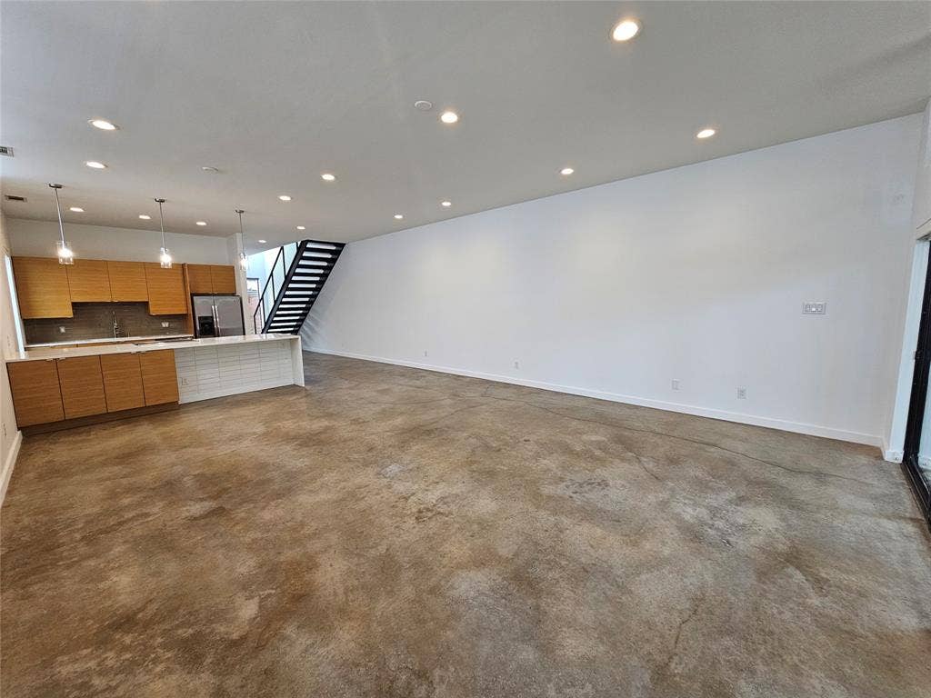 4215 Roseland Avenue, Dallas, TX 75204 Open floor plan featuring polished concrete flooring, recessed lighting, horizontal wood-grain cabinetry, and a metal floating staircase