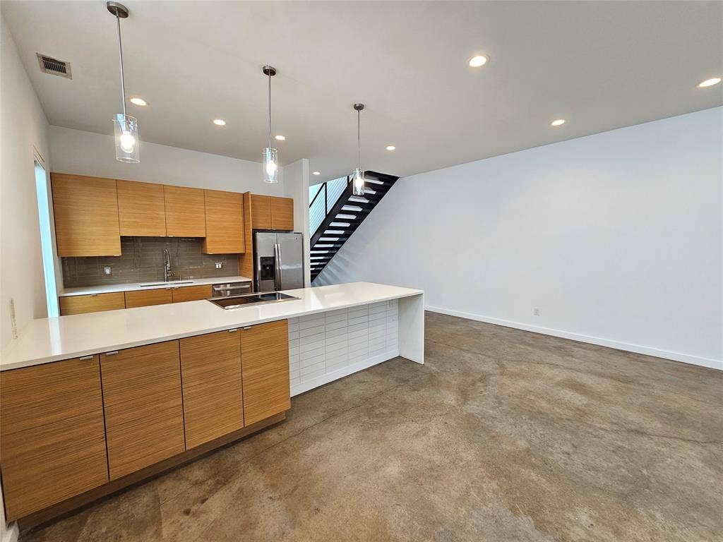 4215 Roseland Avenue, Dallas, TX 75204 Modern kitchen featuring flat-panel wood-finish cabinetry, a large quartz-topped island with an integrated cooktop, polished concrete flooring, recessed lighting, and glass pendant fixtures