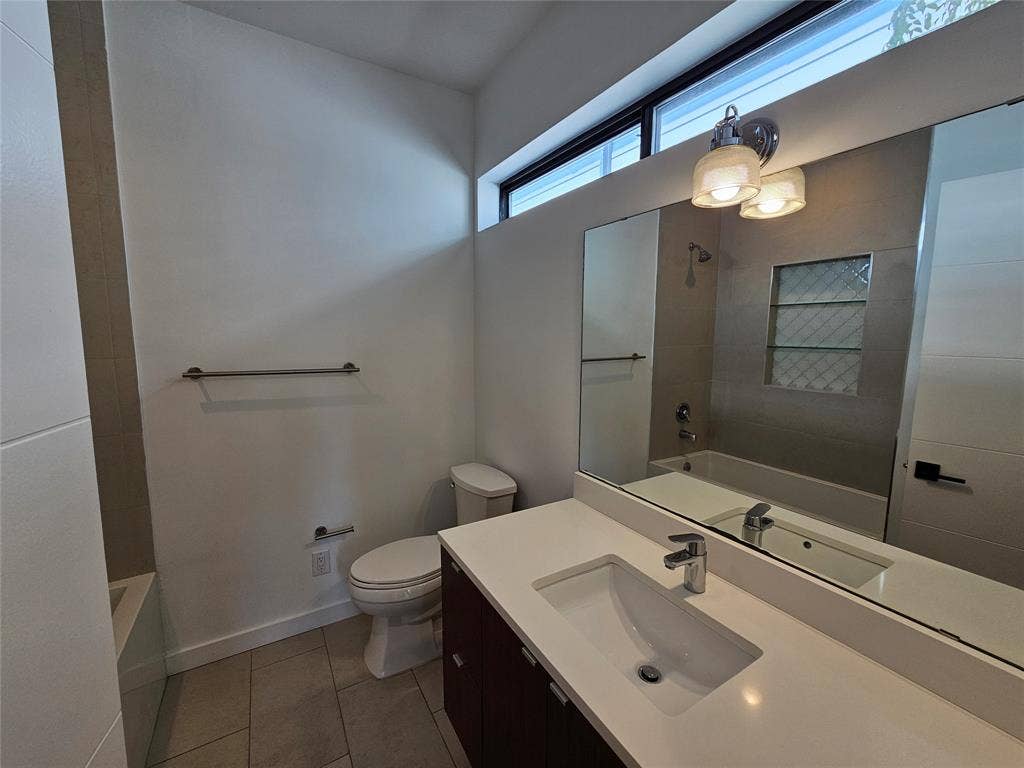 4215 Roseland Avenue, Dallas, TX 75204 Dark wood-finish vanity with a white countertop and integrated sink, large wall-mounted mirror, transom window, and built-in tiled shower niche