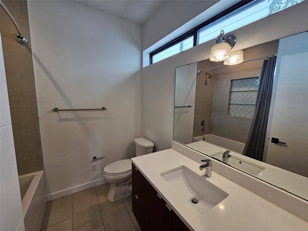 4215 Roseland Avenue, Dallas, TX 75204 Bathroom featuring a dual-tone vanity with a white countertop, an undermount sink, a large wall-mounted mirror, transom window, and a bathtub with tile surround