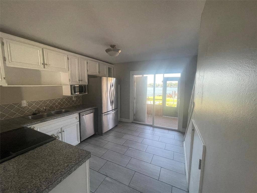 Kitchen with appliances with stainless steel finishes, backsplash, white cabinetry, and sink