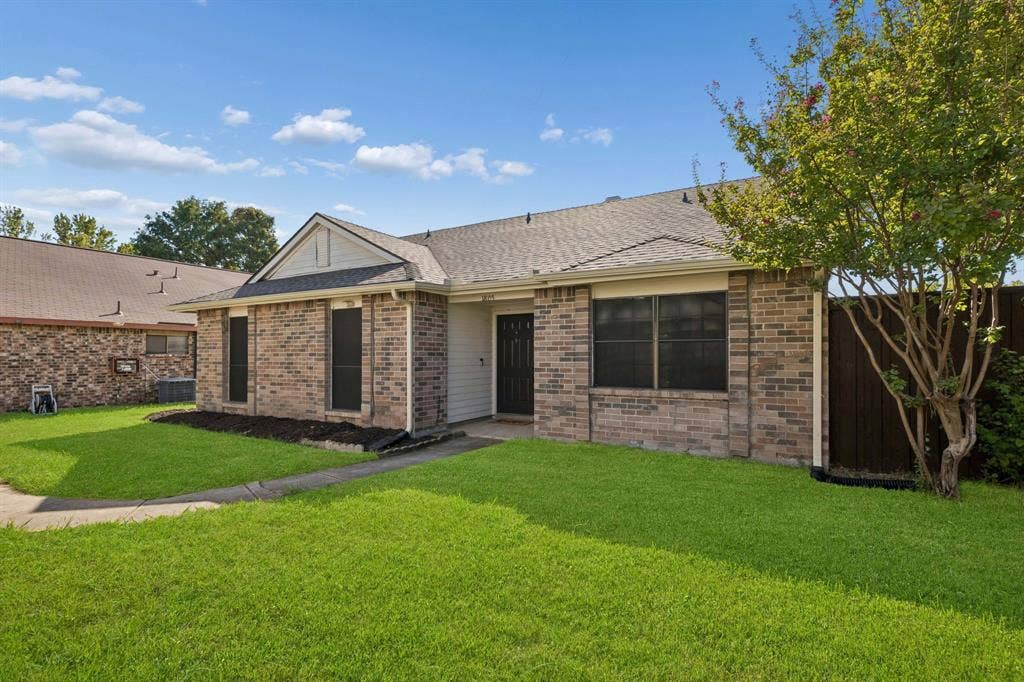 Single-story residence featuring a brick veneer exterior, shingle roofing, concrete walkway, and landscaped garden beds