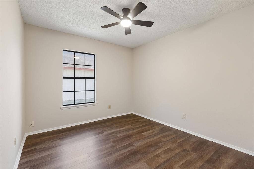 Neutral-toned interior space featuring wood-finish flooring, a multi-pane window with dark trim, and a centralized ceiling fan with integrated lighting