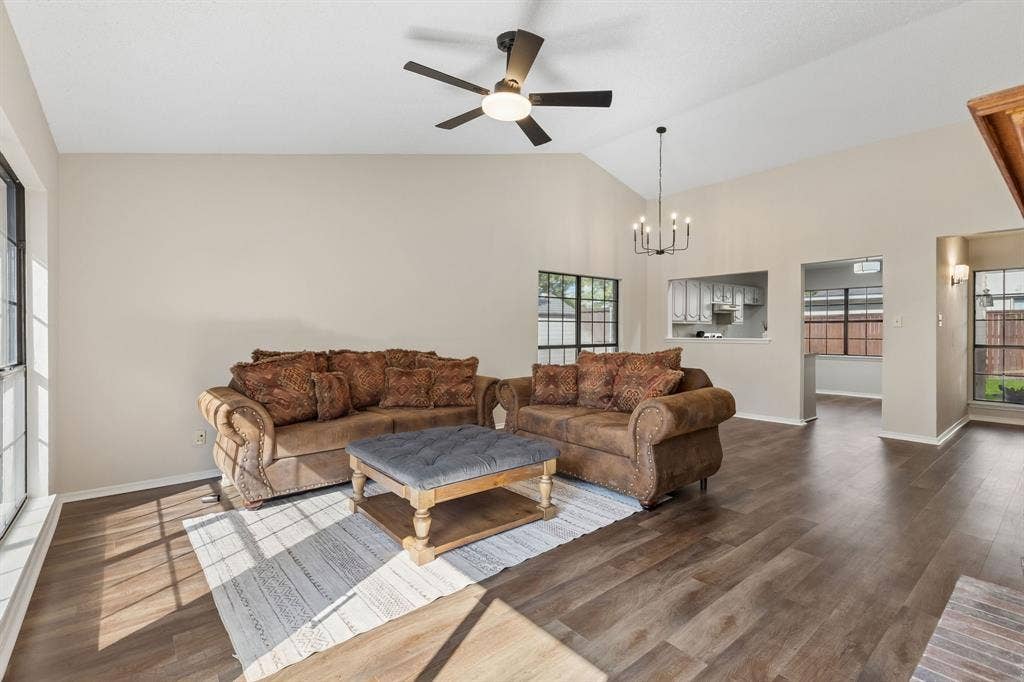 Vaulted ceilings featuring a ceiling fan and a multi-light chandelier, complemented by wood-finish flooring and expansive windows