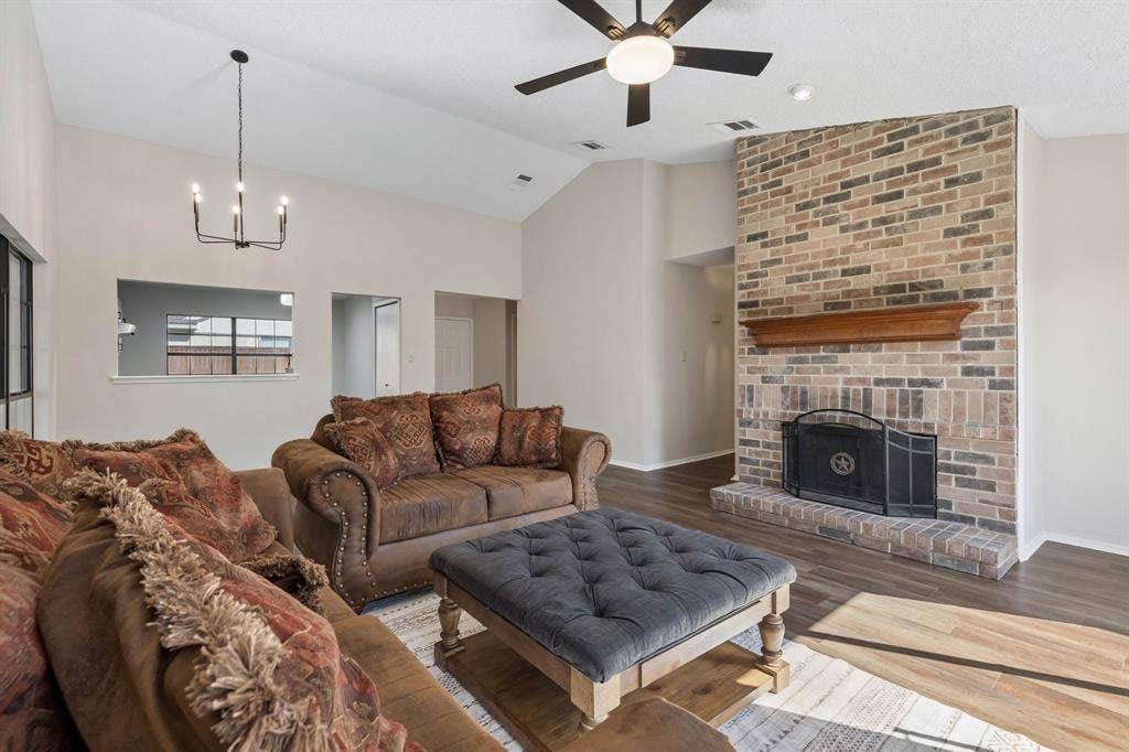 Vaulted ceiling featuring a full-height brick fireplace, wood-finish flooring, a tiered metal chandelier, and a ceiling fan