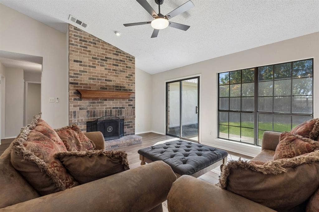 Vaulted ceiling living area featuring a full-height brick fireplace, wood mantel, grid-pattern windows, and sliding glass door