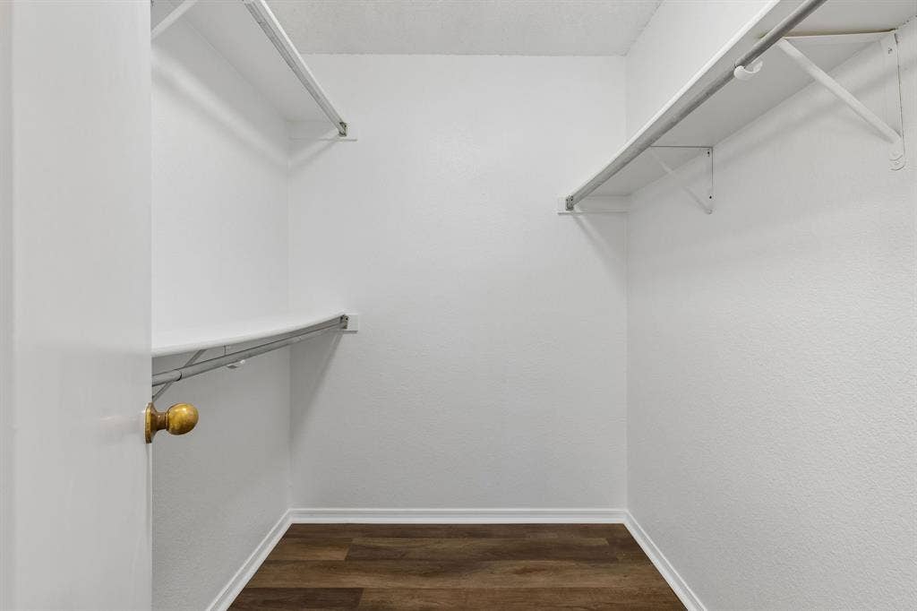 Walk-in closet featuring wood-finish flooring, white walls, and dual-level shelving with integrated clothing rods
