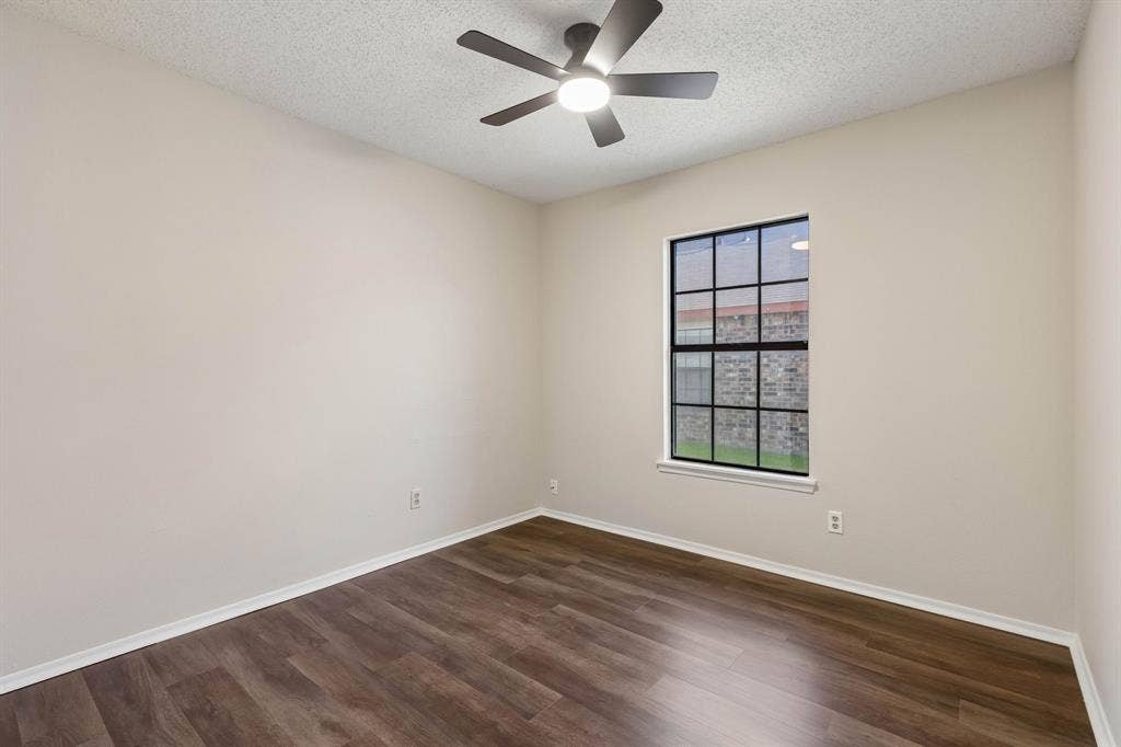 Wood-finish flooring, neutral wall tones, multi-pane window with black frame, and ceiling fan with integrated lighting