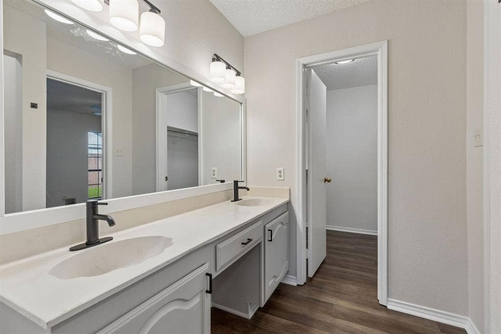 Dual-sink vanity with matte black fixtures, solid-surface countertop, full-width vanity mirror, and wood-finish flooring