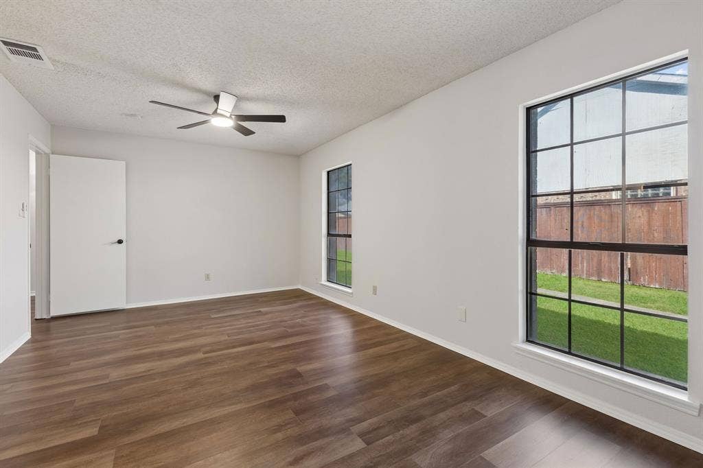 Interior space featuring wood-finish flooring, dual windows with black frames, and a ceiling-mounted light fixture with a multi-blade fan