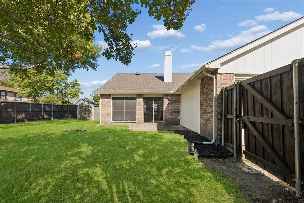 Rear exterior featuring brick siding, a vertical chimney, a concrete patio, and a wood privacy fence enclosing the lawn