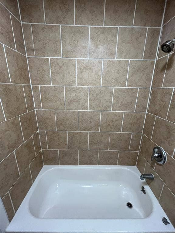 Bathtub surround featuring square, neutral-toned tile with contrasting grout lines, chrome showerhead, and matching chrome faucet assembly
