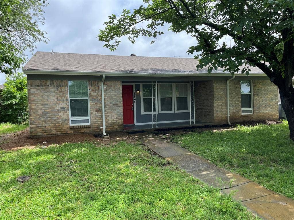 Single-story brick exterior featuring a recessed front porch, metal support columns, a vibrant red entry door, and a concrete walkway