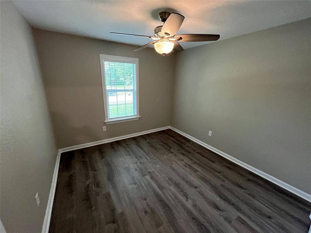 Room featuring wood-finish flooring, neutral wall paint, and a ceiling fan with integrated lighting, centered by a single window with blinds