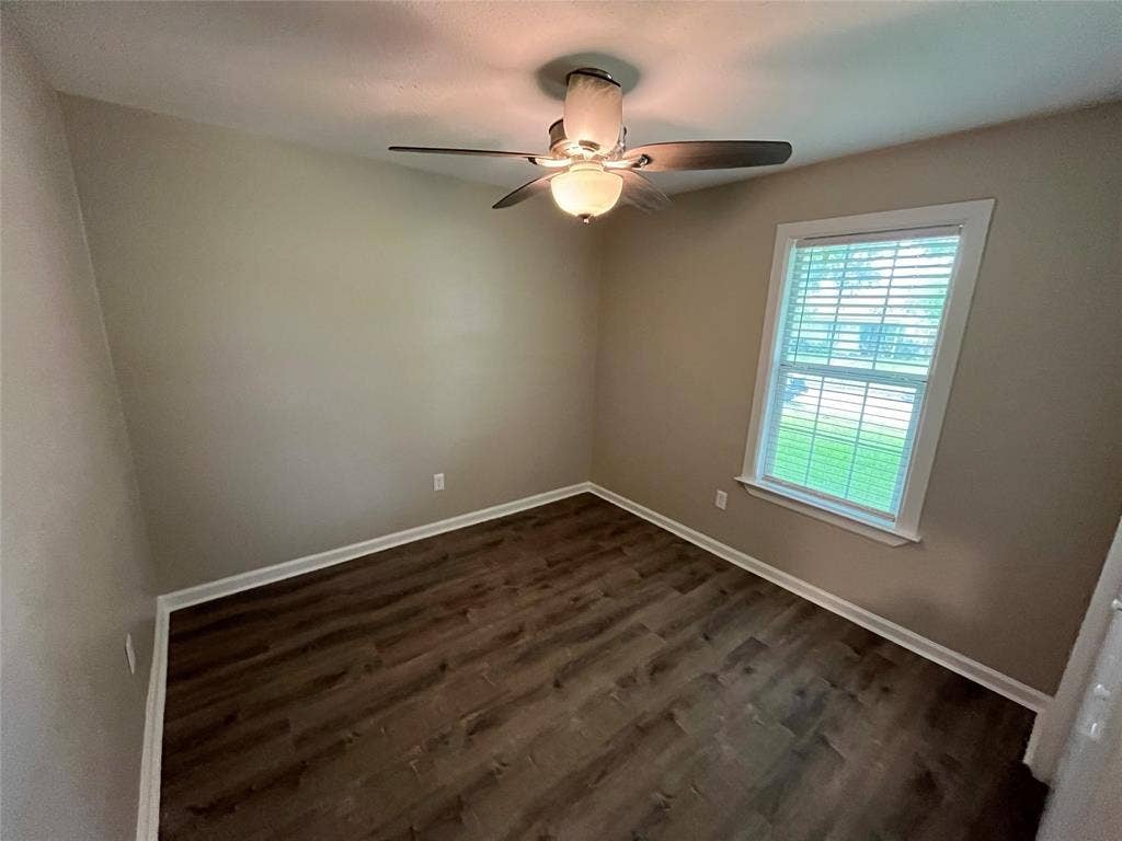 Wood-finish flooring, multi-pane window with horizontal blinds, and a multi-blade ceiling fan featuring integrated dual light fixtures